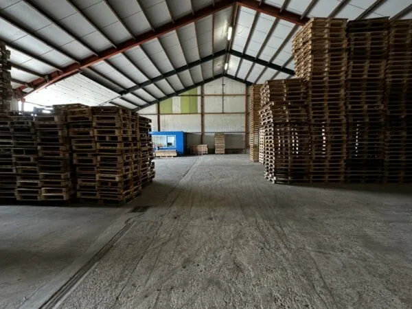 Grote opslagloods aan de Graaf van Lynden van Sandenburgweg met hoge stapels houten pallets en een blauwe containerunit.